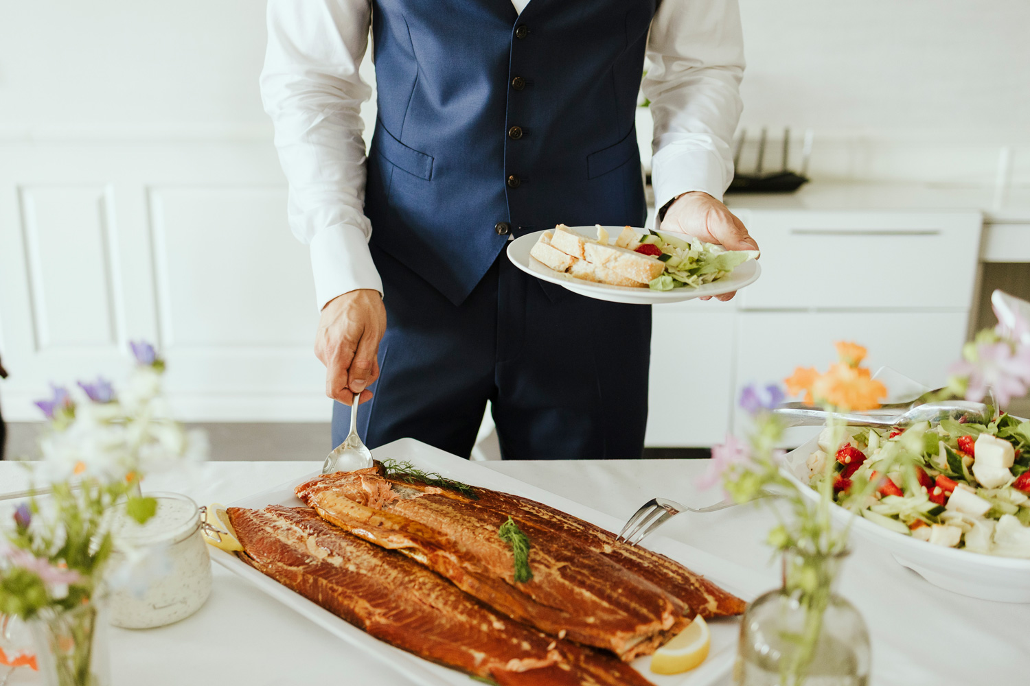 Juhlavieras annostelee isoilta vadilta lohta lautaselleen buffetpöydän äärellä.